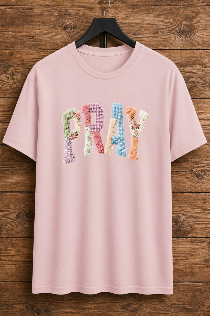 Light Pink t-shirt with floral 'PRAY' text on a wooden background